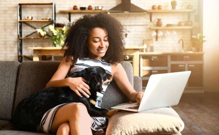 Beautiful African-American woman with cute dog working on WiFi at home